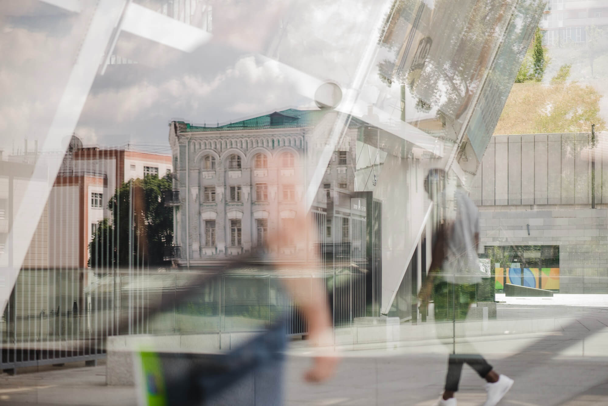 Blurred reflections of people walking and city buildings on glass in an urban setting.